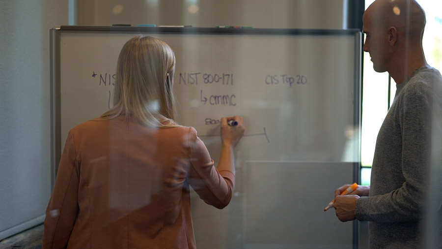 Woman and man brainstorming cybersecurity frameworks at a whiteboard.