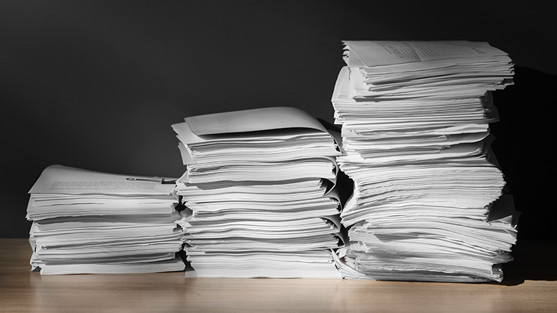 Three piles of paper documents on a tabletop, representing the physical documents that a document imaging system can help businesses digitize and manage electronically.