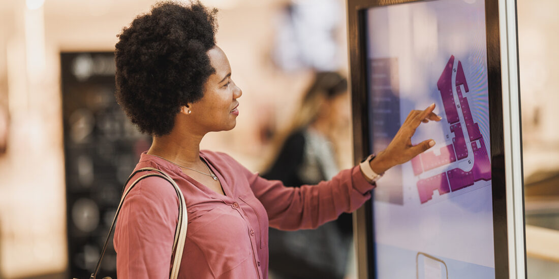 A shopper engages with an interactive digital signage kiosk, showcasing best practices in digital signage with its user-friendly interface and clear, vibrant graphics that enhance the customer experience in a modern retail setting.