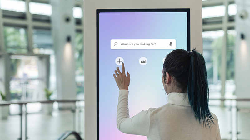 A user engages with an interactive digital signage display featuring a clear and intuitive interface, highlighting best practices in digital signage by offering an accessible and seamless user experience in a modern indoor setting.