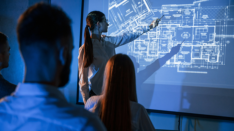 A team attentively reviews architectural plans presented on a large digital signage screen, exemplifying best practices in digital signage through the use of high-resolution displays for collaborative and detailed planning sessions.