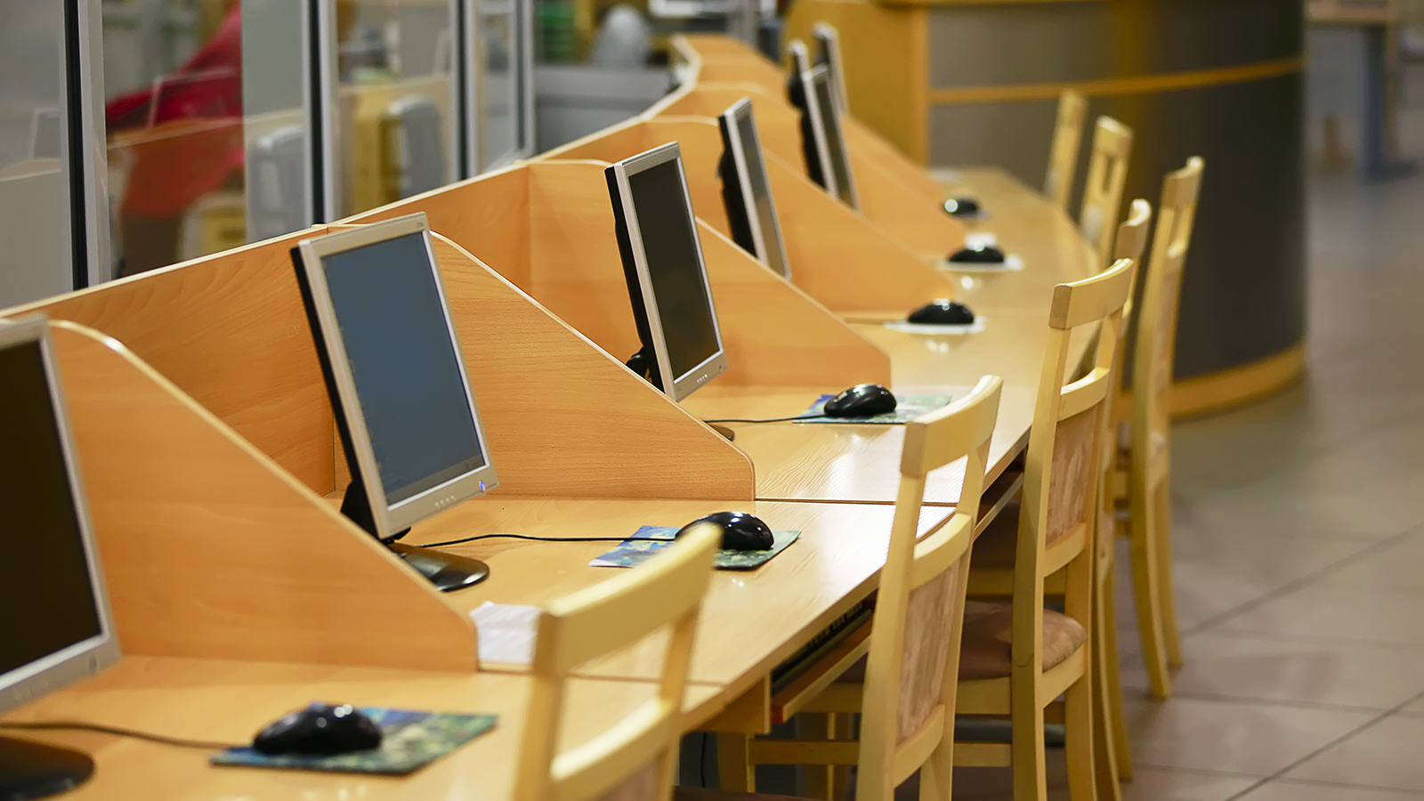 Computer monitors sit on wooden desks with a mouse and mouse pad, as well as wooden chairs. Computer monitors sit on wooden desks with a mouse and mouse pad, as well as wooden chairs.