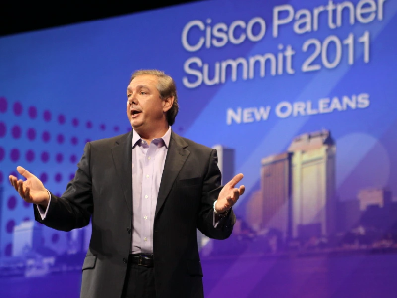 Man in suite presenting in front of the 2011 Cisco Partner Summit banner where HBS was named HBS is named Cisco Partner of the Year.