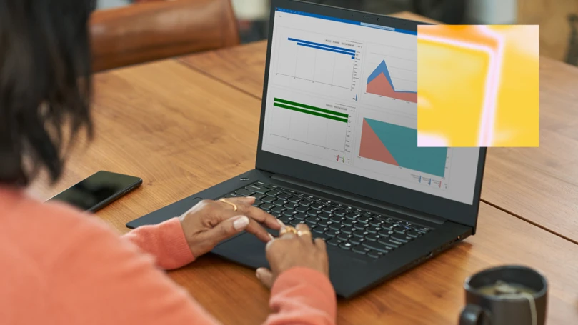 Microsoft Purview. photo of person with back turned to camera and mostly off screen sitting at a table and using a laptop to look at graphs on screen