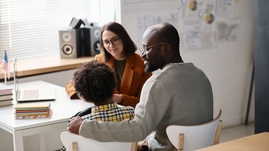 young caucasian teacher talking to an african american father and his young son in a classroom setting