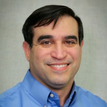 Smiling man in a light blue button-down shirt facing the camera (portrait).