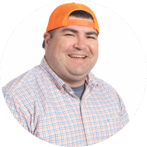 Cheerful man wearing an orange backward baseball cap and a light plaid shirt, smiling at the camera against a white background.