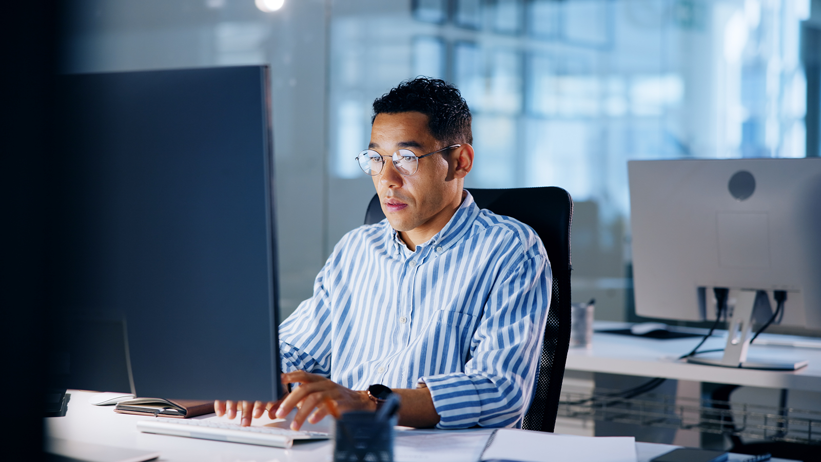 Man in a striped shirt typing at a desktop computer in a bright, modern office.] , hmm fix