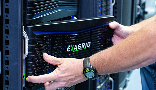Technician installing or securing an ExaGRID storage appliance in a server rack in a data center.